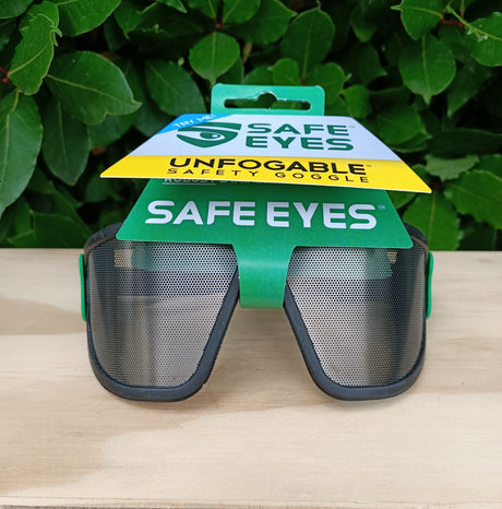 Safe Eyes safety goggles with packaging on a wooden surface and green leafy background